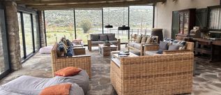 Gemütliche Lounge mit Korbsofas, Sitzsäcken, Holzbalkendecke und großen Fenstern zur Landschaft.