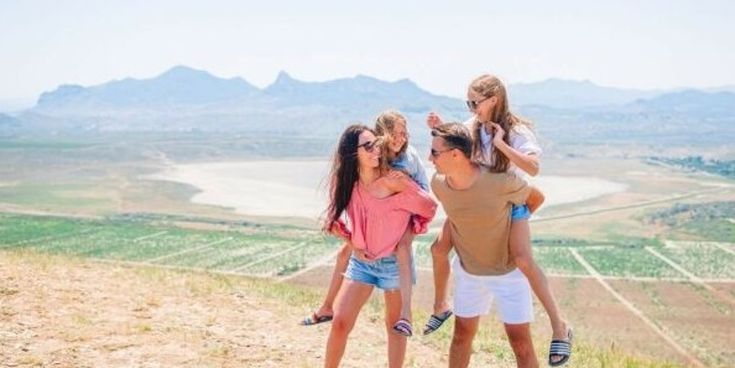 Fröhliche Familie mit zwei Kindern genießt gemeinsam die Aussicht auf eine weite Landschaft – Symbol für Familienreisen und gemeinsame Abenteuer.