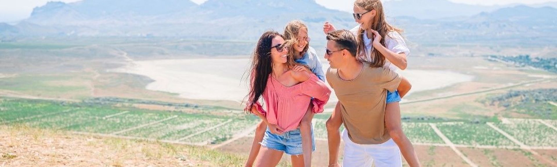 Fröhliche Familie mit zwei Kindern genießt gemeinsam die Aussicht auf eine weite Landschaft – Symbol für Familienreisen und gemeinsame Abenteuer.