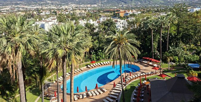 Blick über den geschwungenen Pool und den tropischen Garten des Hotel Botánico bis zu den grünen Berghängen Teneriffas.