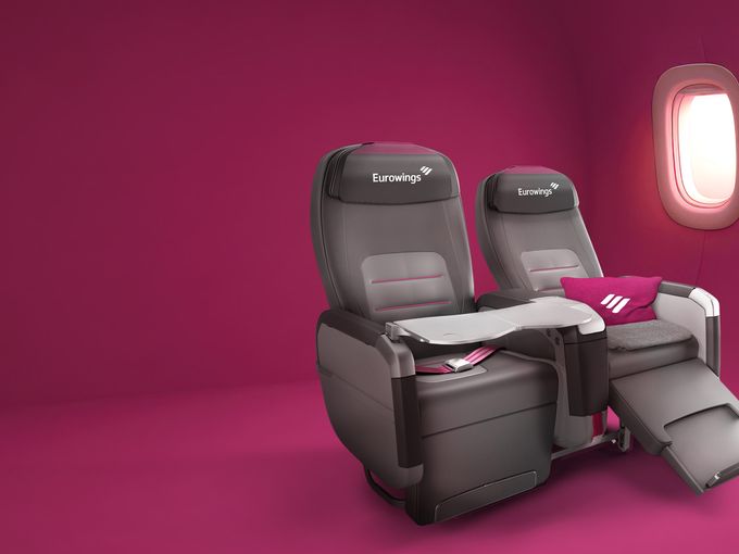 Eurowings-BIZclass-Sitz in Liegeposition mit Kissen und Decke vor pinkfarbenem Hintergrund
