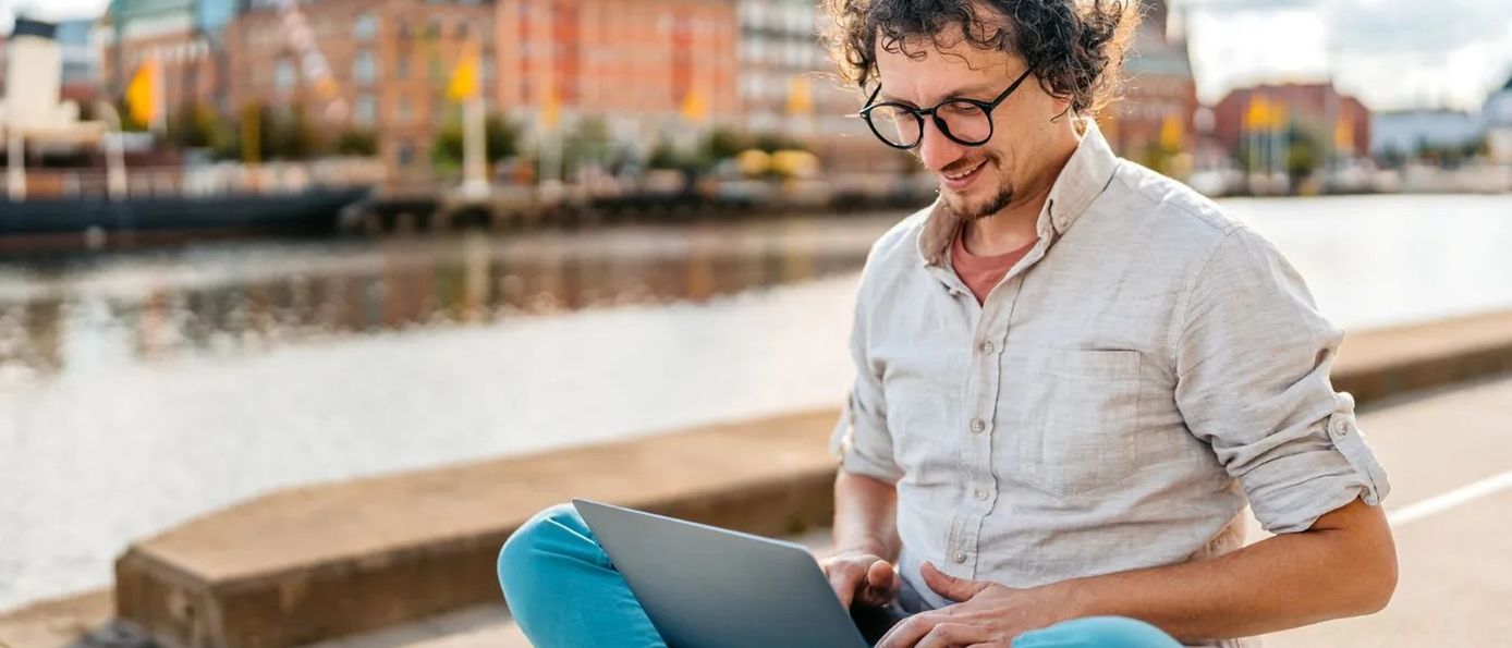 Mann arbeitet mit Laptop am Wasser in einer Stadt