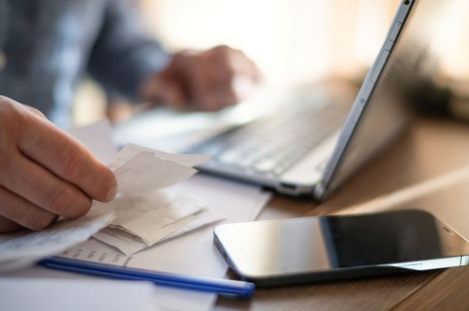 Geschäftsreisender prüft Belege neben Laptop und Smartphone