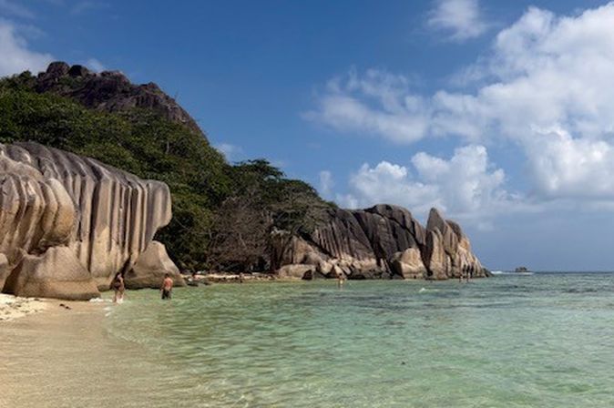 Flache, türkisfarbene Bucht mit markanten Granitfelsen und zwei Personen am Strand.