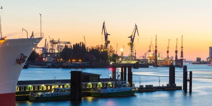 Blick auf den Hamburger Hafen bei Sonnenuntergang mit Schiffen, Kränen und ruhigem Wasser unter farbigem Abendhimmel.