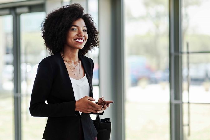 Person in Businesskleidung steht in einem hellen Gebäude und hält ein Smartphone in der Hand.