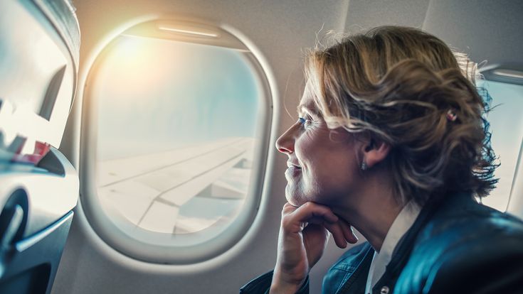 Frau sieht lächelnd aus dem Fenster eines Flugzeugs