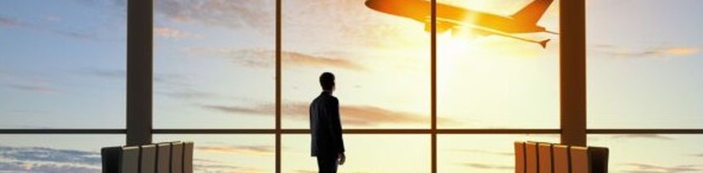 Reisender beobachtet durch die Glasfassade eines Flughafens den Start eines Flugzeugs bei Sonnenuntergang.