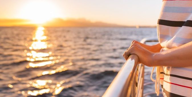 Eine Person steht an der Reling und schaut auf den goldenen Sonnenuntergang über dem Meer.