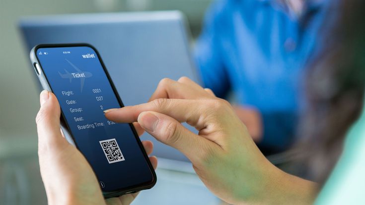 Eine Frau scannt mit ihrem Smartphone einen QR-Code auf einem Bildschirm oder Ticket.