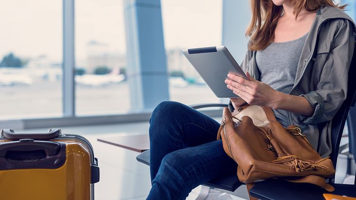 Frau mit Laptop, Tasche und Trolley am Flughafen