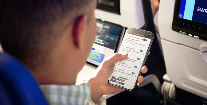 Mann an Bord von United Airlines mit Smartphone in der Hand und das Display zeigt die App / Wifi
