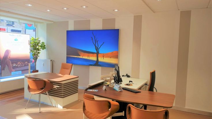 Reisebüro-Arbeitsplatz mit großem Bildschirm, der eine Wüstenlandschaft zeigt, und warm beleuchtetem Beratungsbereich.