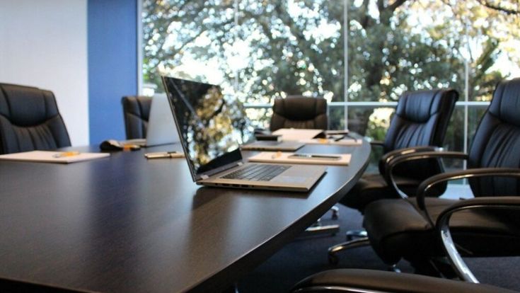 Moderner Konferenzraum mit Laptop und leeren Stühlen vor großen Fenstern – Sinnbild für professionelle Arbeitsumgebung und Geschäftsmeetings.