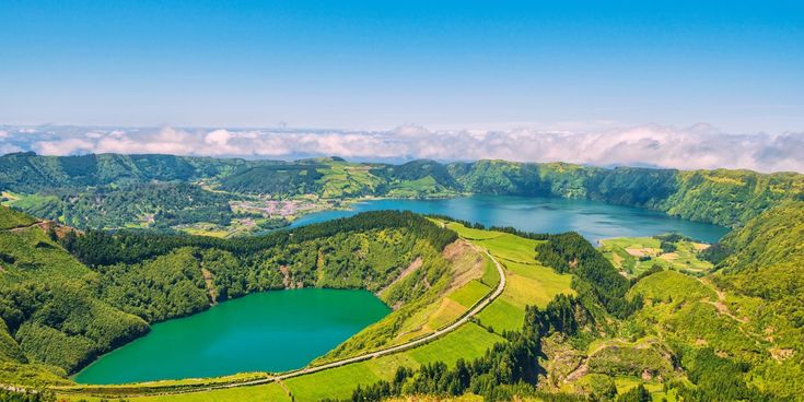Panoramablick auf die grünen Kraterseen der Sete Cidades auf den Azoren, umgeben von bewaldeten Hügeln und Feldern.
