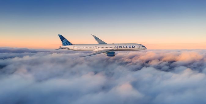 United Airlines Boeing 787 Dreamliner im Seitenprofil über einer Wolkendecke, im Hintergrund ein Sonnenuntergangshimmel.