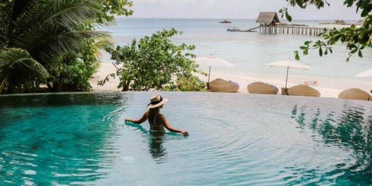 Zwei Personen stoßen mit kühlen Getränken am Strand bei Sonnenuntergang an – Symbol für Entspannung und Urlaubsfeeling.