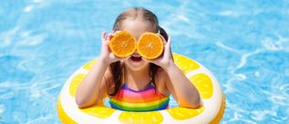 Mädchen in einem Zitronen-Schwimmring hält zwei Orangenhälften vor die Augen.