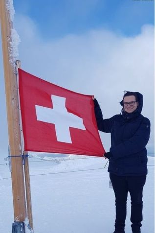 Mann hält am Berggipfel Schweizer Fahne