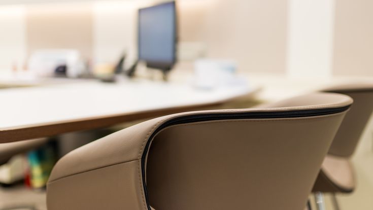 Detailaufnahme eines modernen Beratungsstuhls an einem Schreibtisch mit Computer im unscharfen Hintergrund.