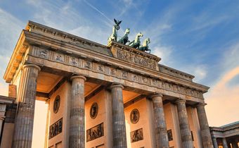 Das Brandenburger Tor in Berlin bei Abendlicht mit goldener Fassade und blauem Himmel im Hintergrund.