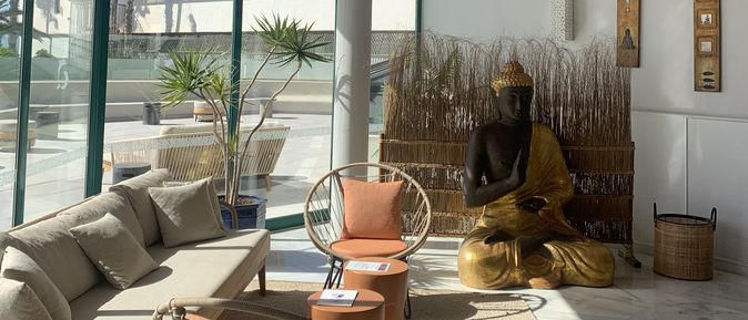 Heller Wellnessbereich mit Sitzmöbeln, großen Fensterfronten und einer goldenen Buddha-Statue.