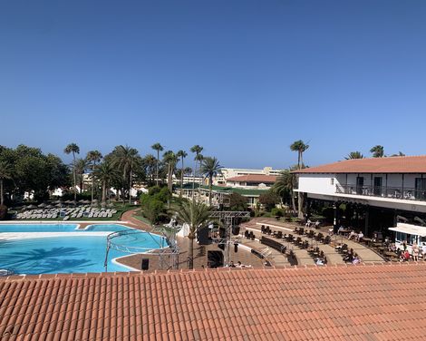 Blick über den großen Pool, die Sonnenterrasse und die palmengesäumte Anlage des Aldiana Clubs.