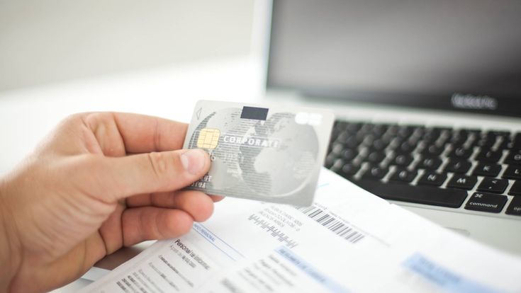 Hand hält Kreditkarte über Laptop-Tastatur, Online-Bezahlung oder Buchung.