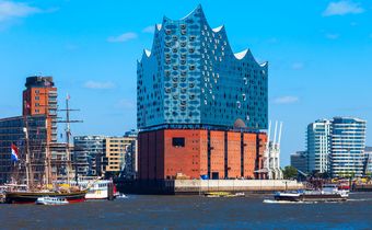 Blick auf die Elbphilharmonie in Hamburg mit vorbeifahrenden Schiffen im Hafen bei strahlend blauem Himmel.