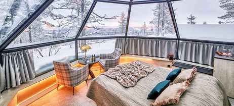 Gemütliches Schlafzimmer in einem Glasiglu mit Panoramablick auf eine verschneite Winterlandschaft bei Tageslicht