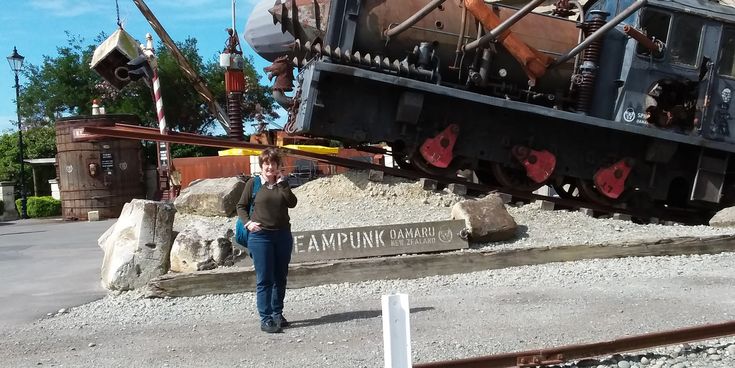 Petra Meyers steht vor einer schräg montierten alten Dampflok im Steampunk HQ Museum in Oamaru, Neuseeland.