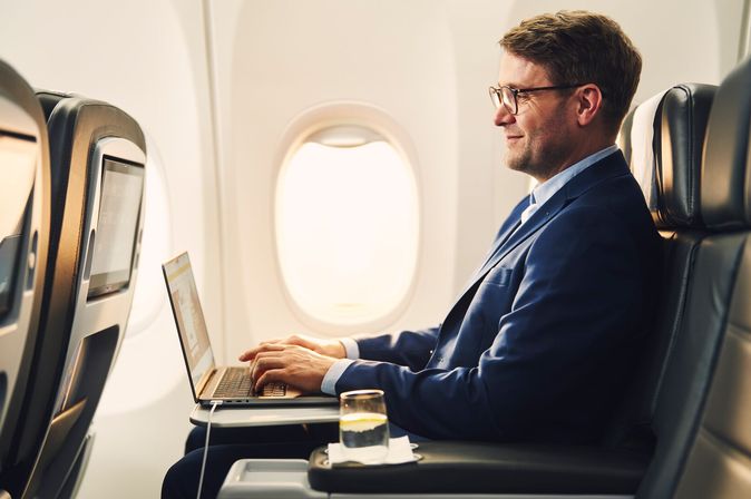 Geschäftsmann im blauen Anzug arbeitet am Laptop in der Business Class eines Flugzeugs.