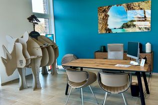 Moderner Beratungsplatz mit Holztisch, bequemen Stühlen und türkisfarbener Akzentwand in der FERNWEHER Reiselounge