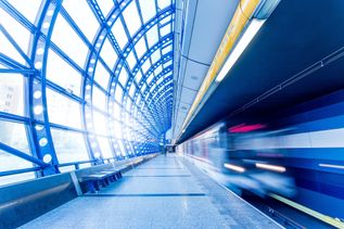 Eine moderne U-Bahn-Station mit blauem Glasdach und einer einfahrenden Bahn in Bewegung.