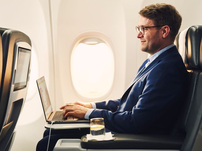 Geschäftsmann im blauen Anzug arbeitet am Laptop in der Business Class eines Flugzeugs.