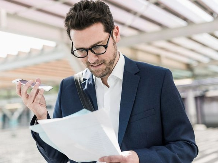 Geschäftsreisender mit Smartphone und Unterlagen in der Hand