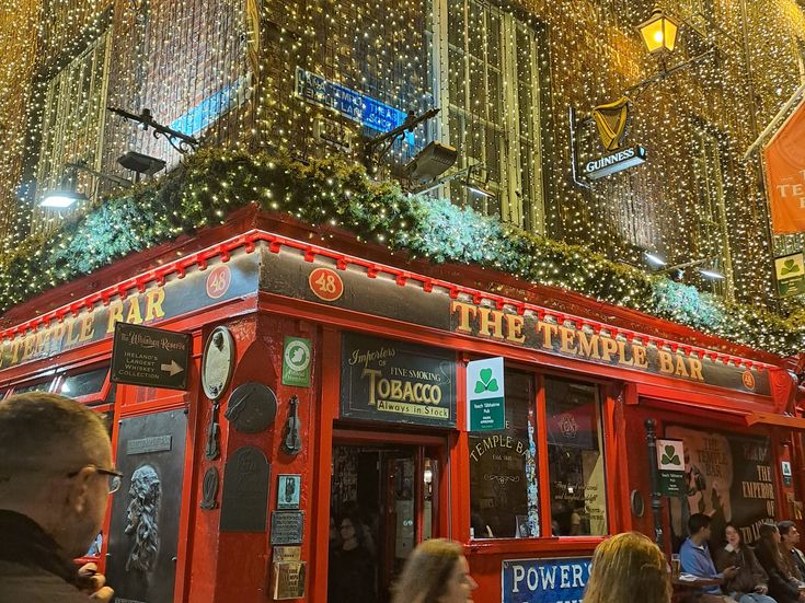 Die rot gestrichene Temple Bar in Dublin bei Nacht, umgeben von festlicher Beleuchtung und zahlreichen Gästen.