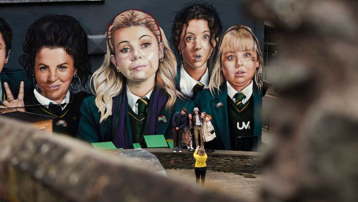 Wandgemälde von vier Personen, das von einer Person in gelber Jacke fotografiert wird