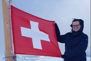 Mann hält am Berggipfel Schweizer Fahne