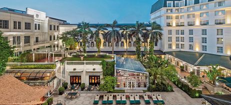 Weißes Hotel mit Bäumen im Vordergrund und leichter Beleuchtung 