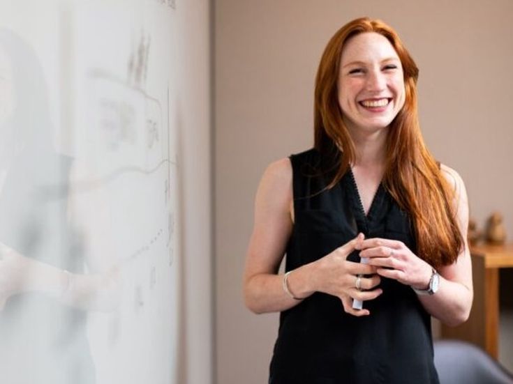 Lächelnde Frau steht vor einem Whiteboard und präsentiert eine Idee während eines Meetings.