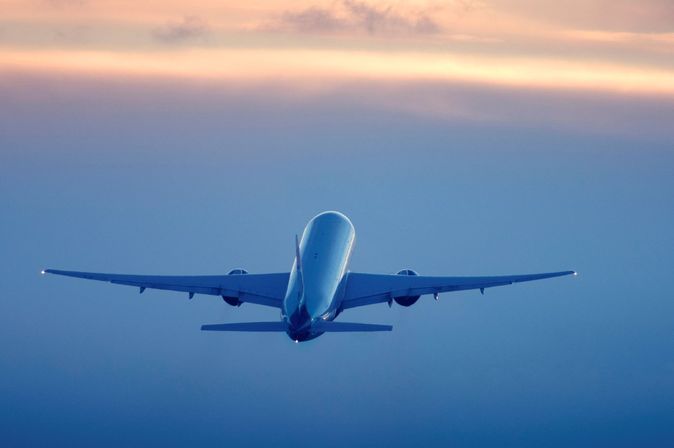 Passagierflugzeug im Steigflug vor farbigem Abendhimmel.