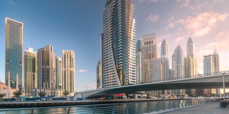 Moderne Skyline mit hohen Wolkenkratzern an einer Uferpromenade bei Sonnenuntergang in einer Wüstenmetropole.