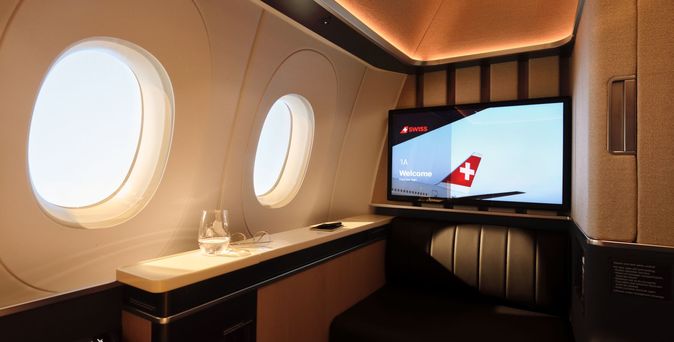 First Class Suite mit zwei Fenstern, Willkommensbildschirm für Sitz 1A und schwarzem Ledersitz.