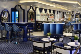 Eine stilvolle, blau-weiß gestaltete Bar-Lounge auf einem Kreuzfahrtschiff mit eleganten Sitzgruppen, langer Theke und dekorativen Details.