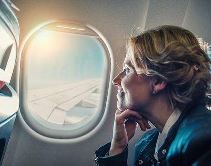 Frau sieht lächelnd aus dem Fenster eines Flugzeugs