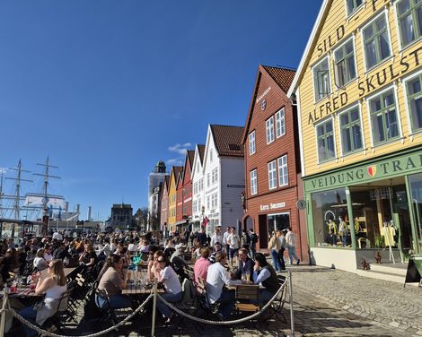 Belebte Uferpromenade am Bryggen mit bunten Holzhäusern und Außengastronomie.