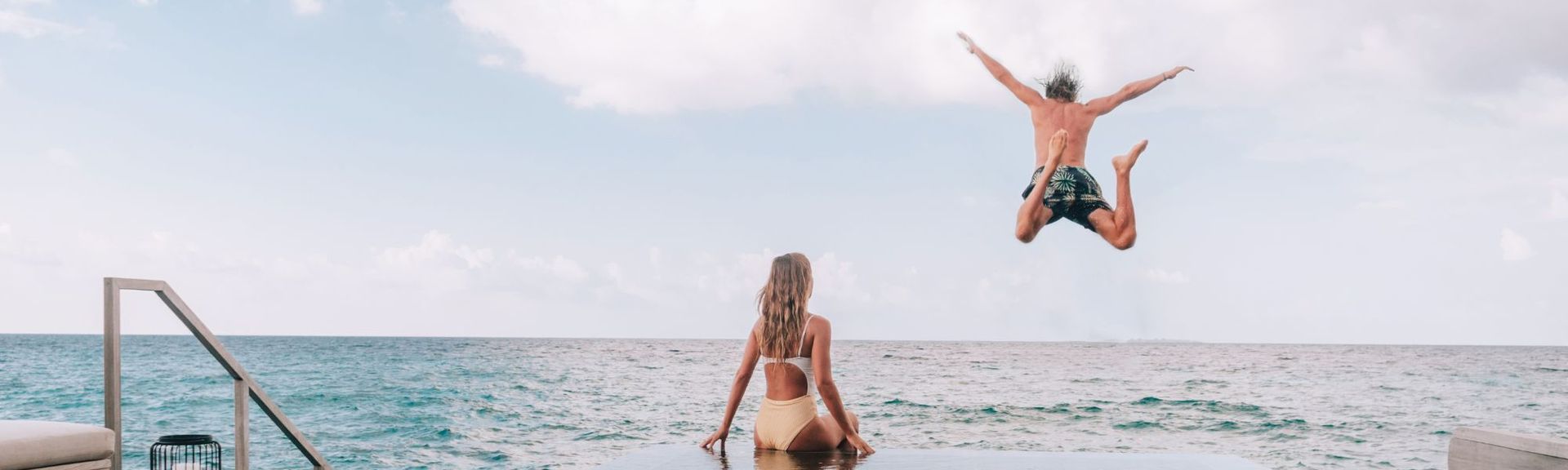 Paar sitzt in einem Cabrio am Strand und blickt in den Sonnenuntergang – Symbol für Freiheit, Reisen und unvergessliche Momente.