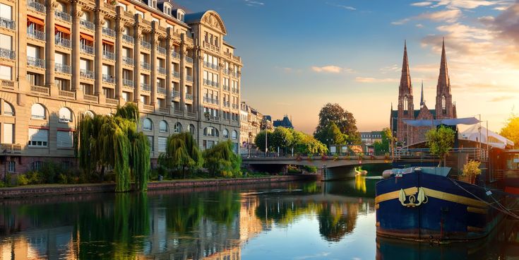 Sonnenuntergang über der Ill in Straßburg mit historischen Gebäuden, Booten und der Kirche Saint-Paul im Hintergrund.