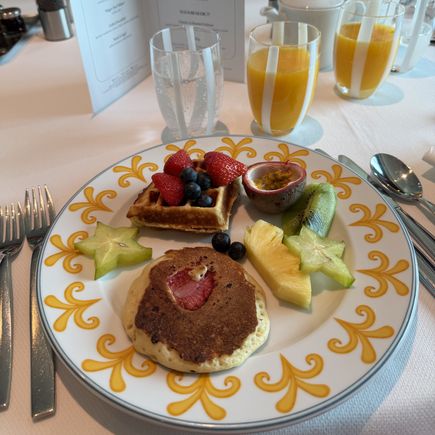 Frühstücksteller mit Pancake, Waffel, Beeren und exotischen Früchten, dazu Orangensaft und Brunchkarte.